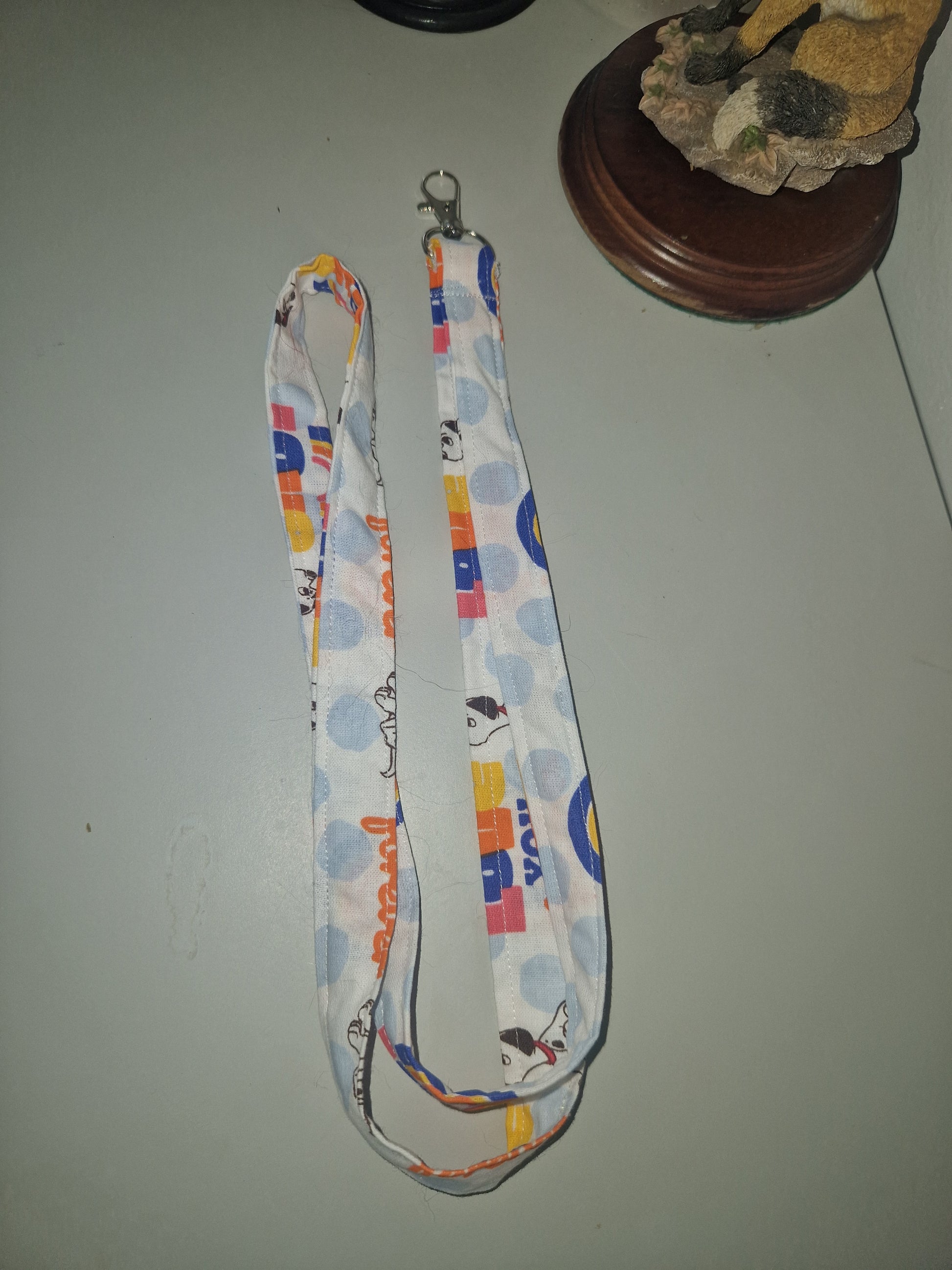 A fabric lanyard strap with a white background, light blue polka dots, and colorful cartoon graphics, laid flat on a gray surface.