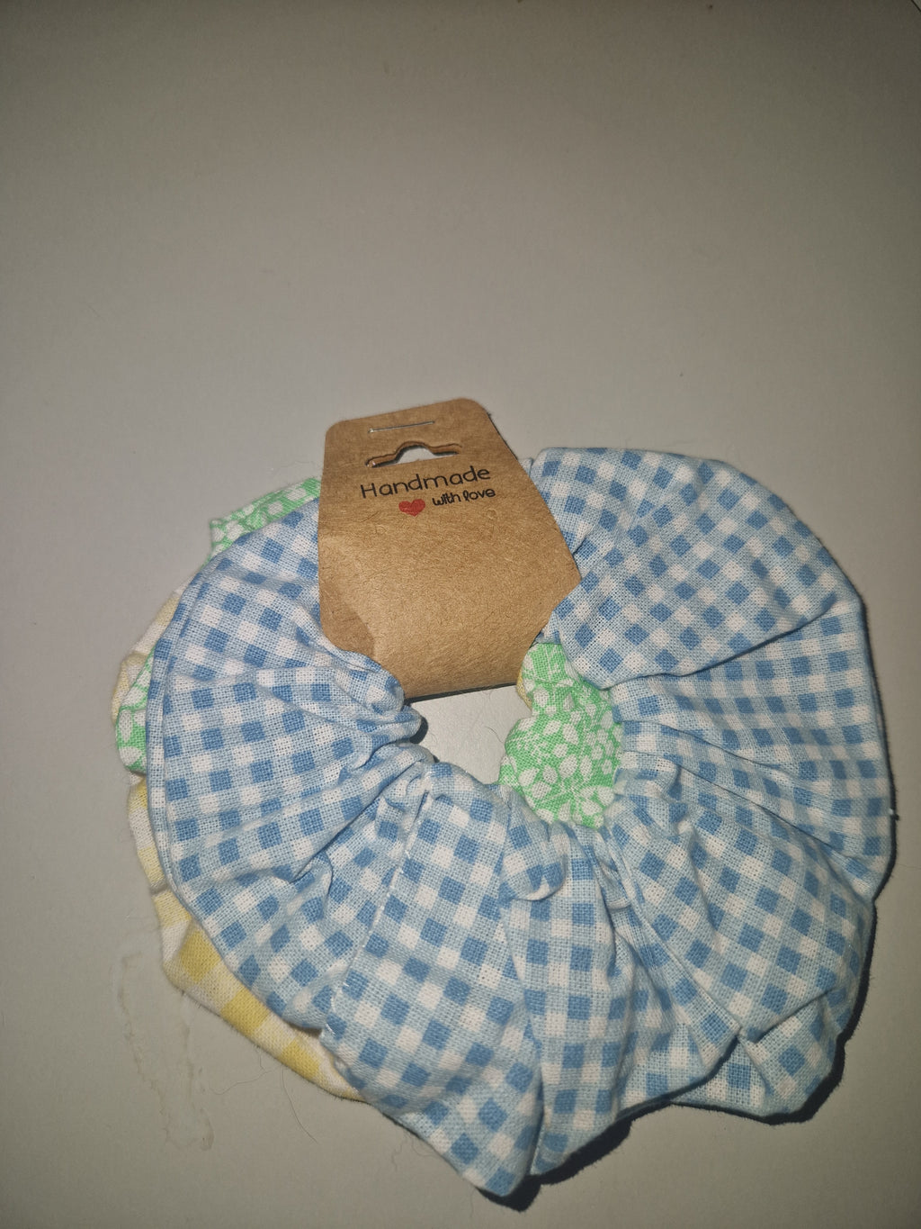 A fabric hair scrunchie with a blue and white gingham pattern, featuring a green patterned inner band and a brown paper tag that reads 'handmade by annie'.