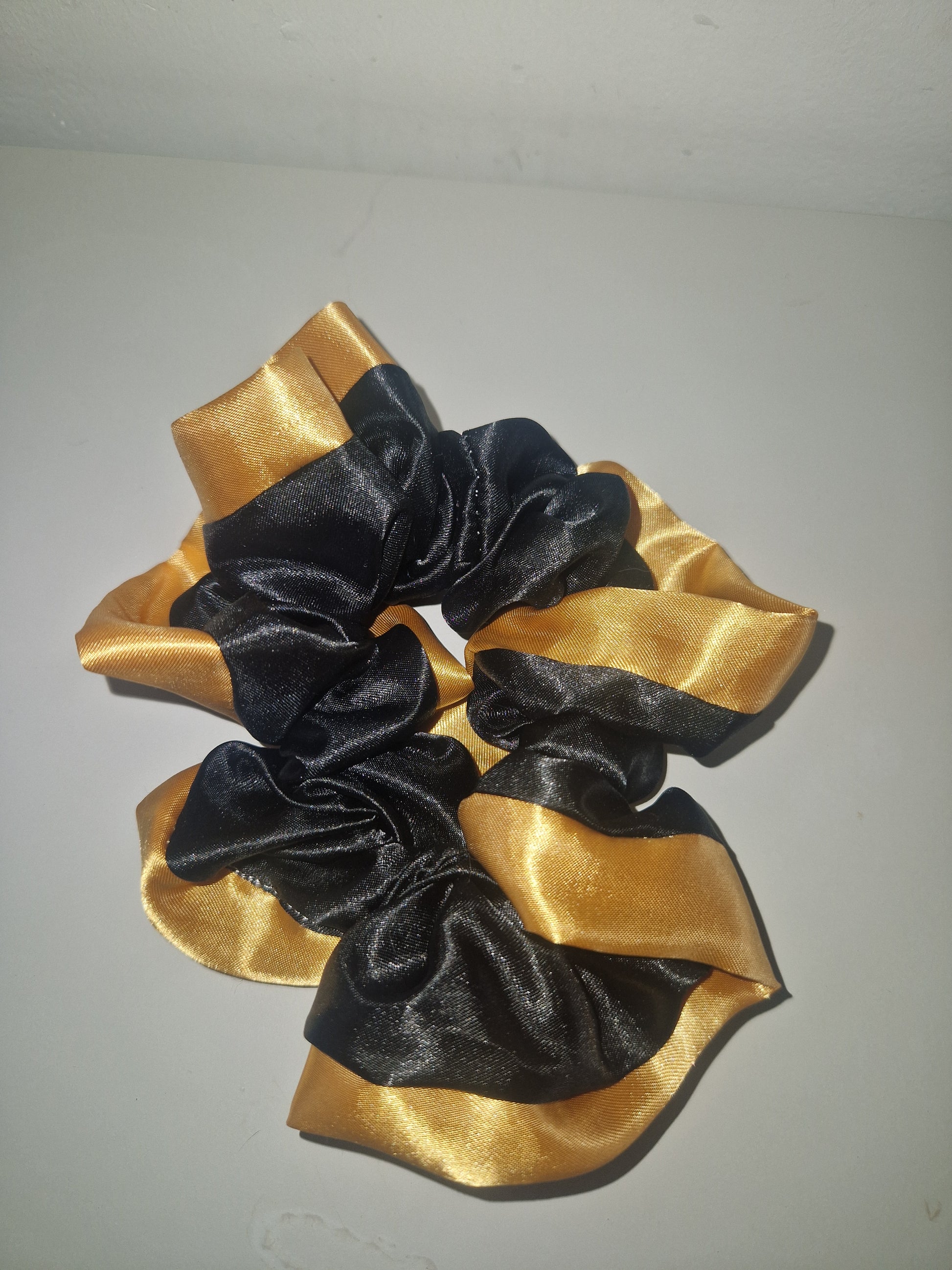 A large hair scrunchie made from alternating wide black and shiny gold satin ribbon loops, shown against a plain light gray background.