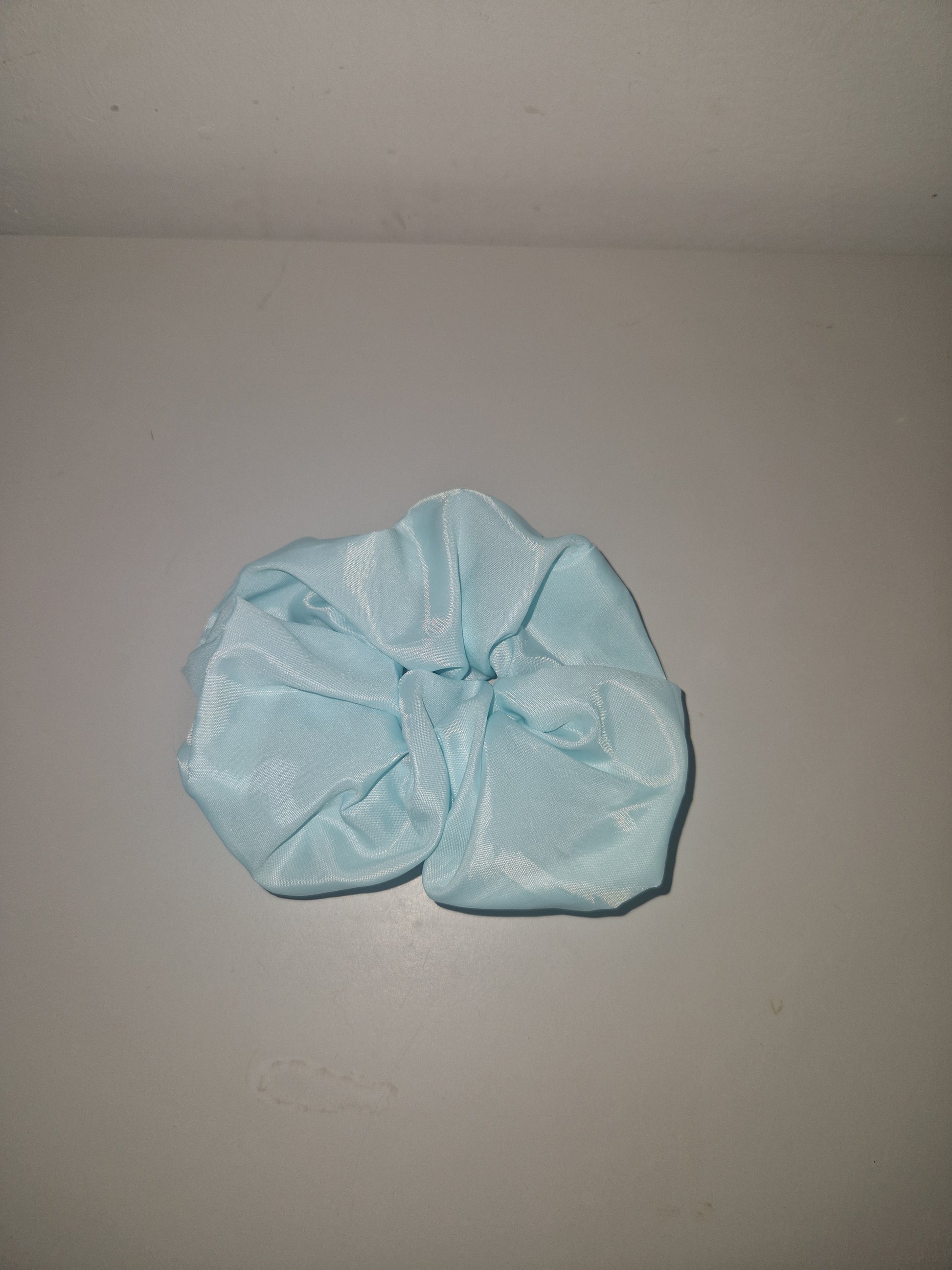 A light blue satin hair scrunchie photographed against a plain beige background.