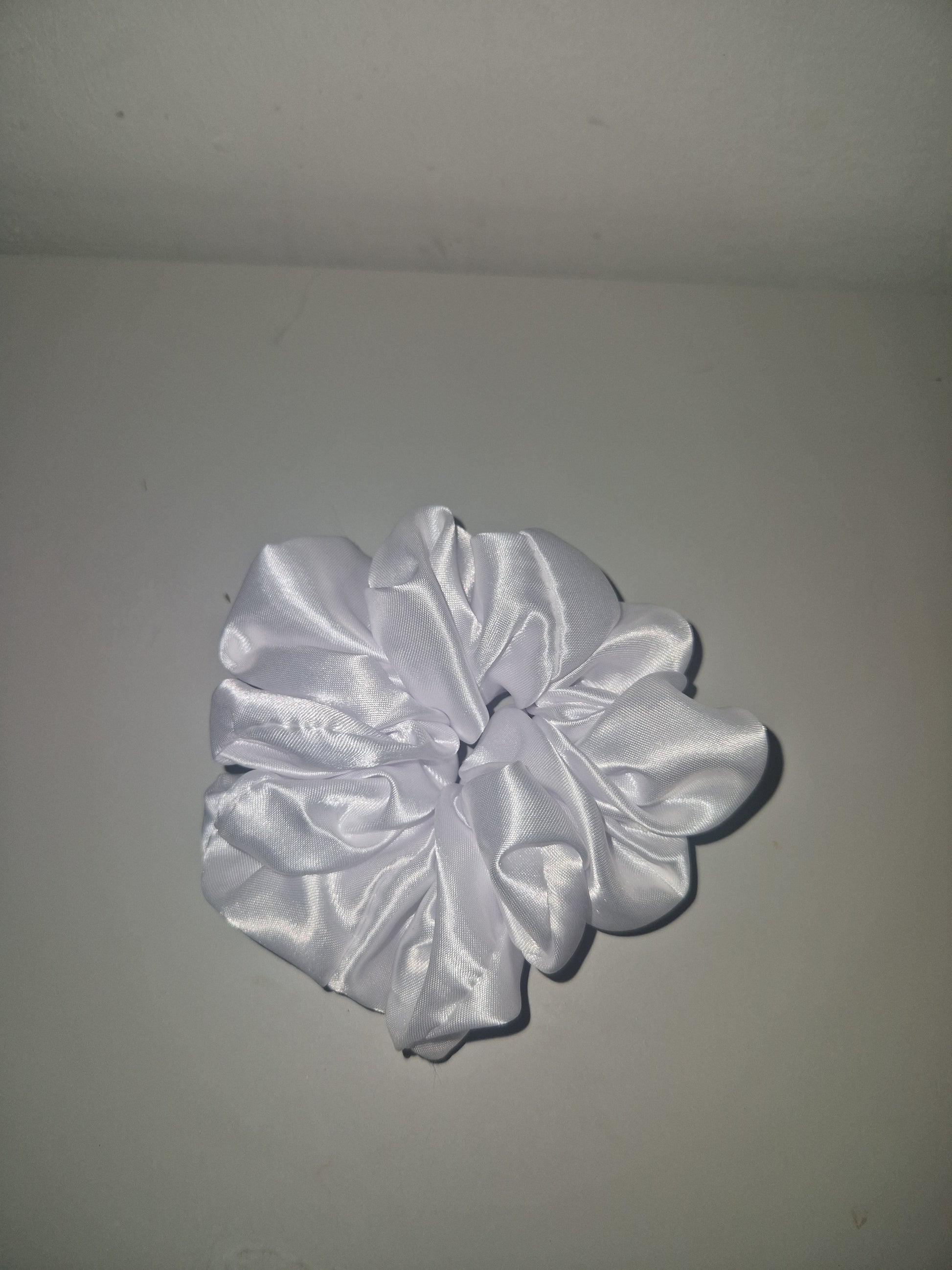 A white satin hair scrunchie with a glossy, shiny finish, photographed against a plain light gray background.