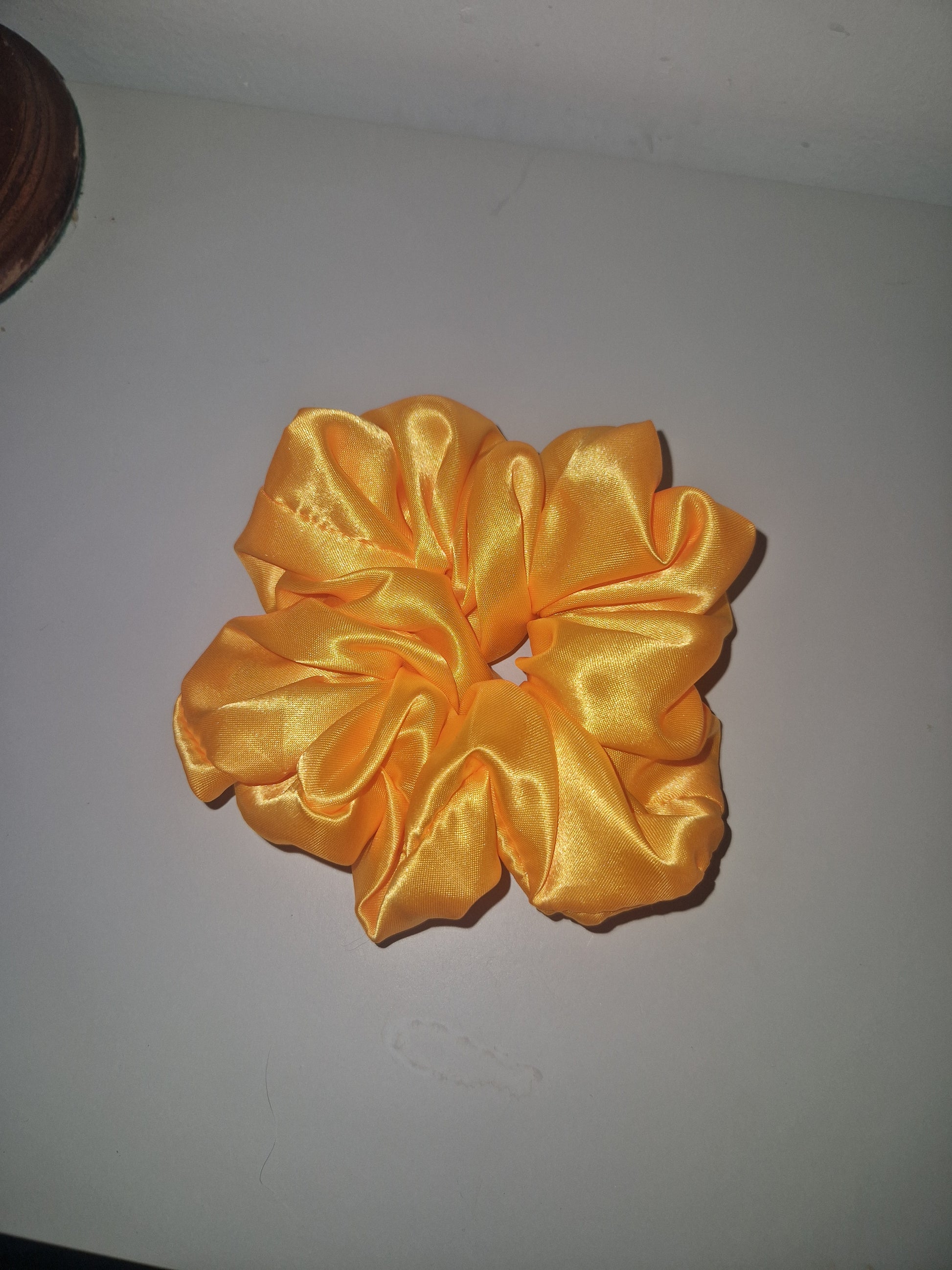 A shiny golden-yellow satin hair scrunchie displayed against a plain light gray background.