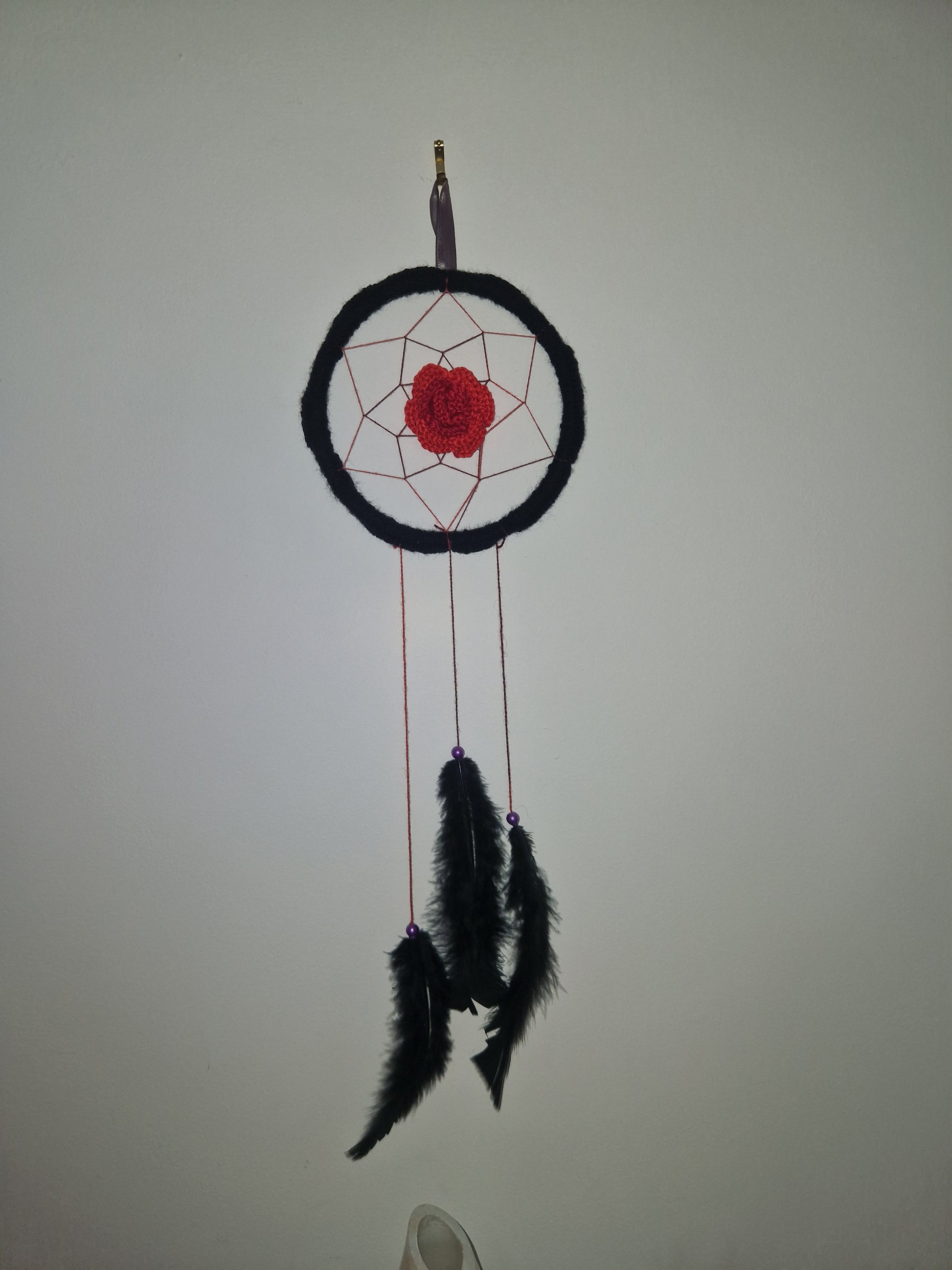 A dreamcatcher wall hanging with a black circular frame, red webbing, a red center, and black feathers on a plain light background.