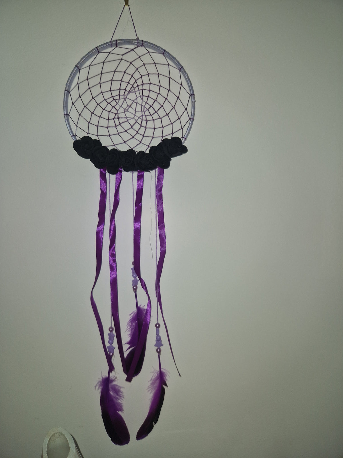 A dreamcatcher-style wall hanging with a circular web frame, purple hanging ribbons, black beads, and purple feathers, photographed against a plain light background.