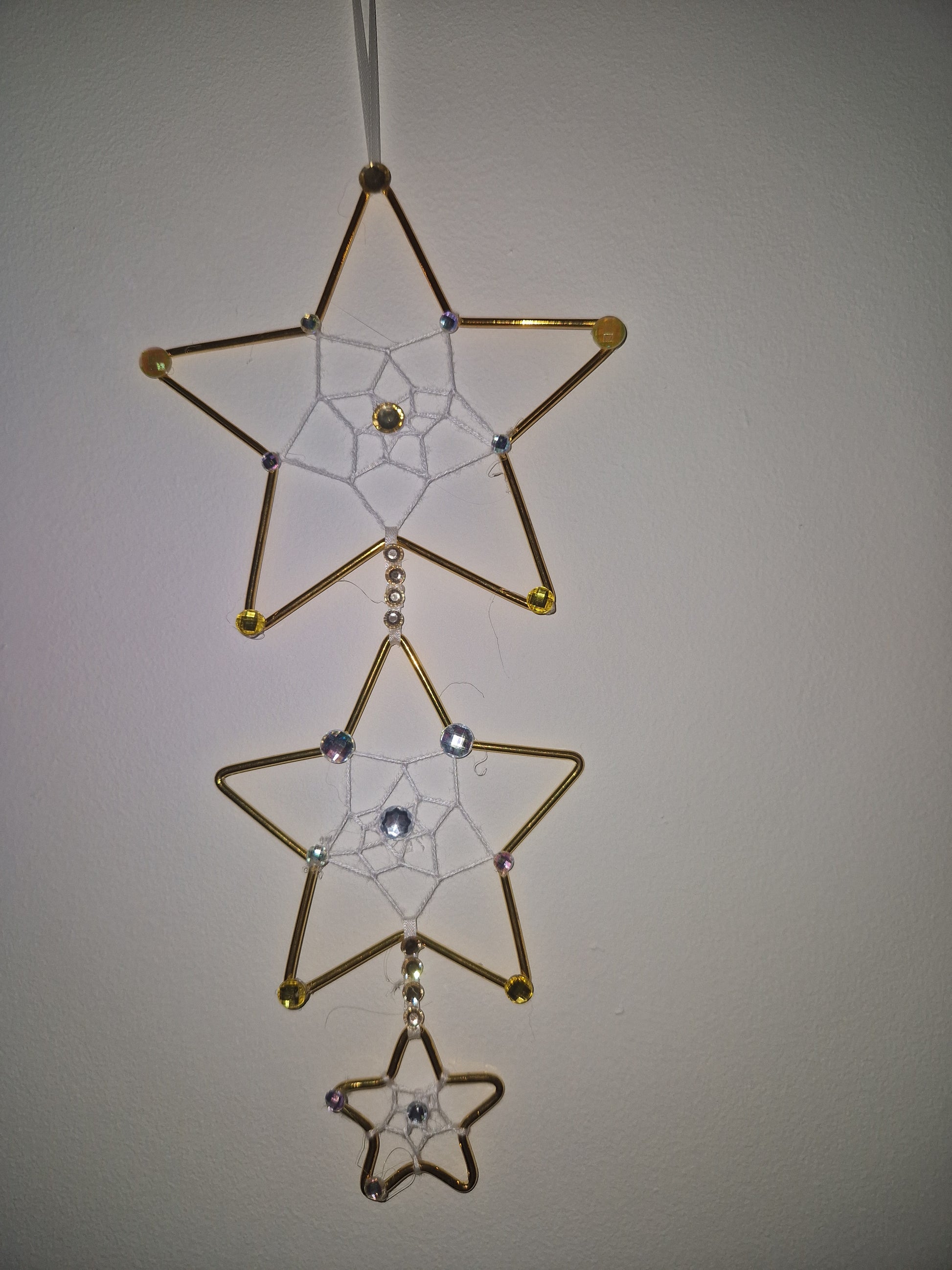 Three gold wire star ornaments with white string webbing and small rhinestone accents, arranged horizontally against a plain light background.