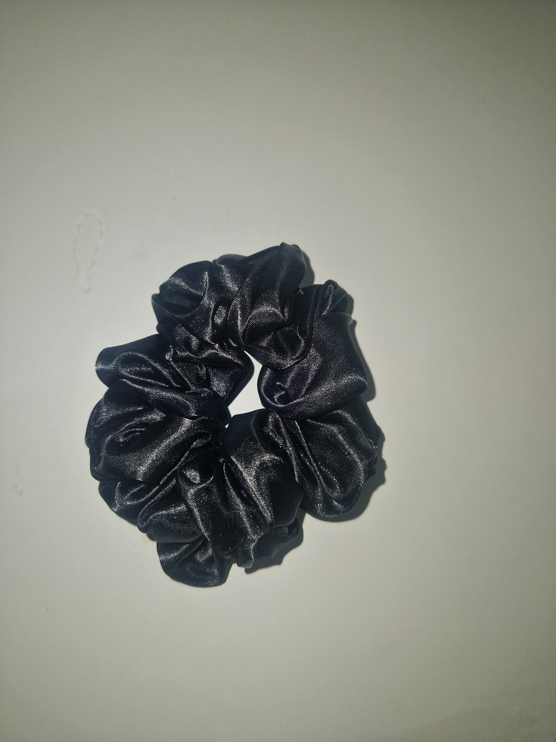 A single black satin or silk scrunchie centered on a plain light gray background.