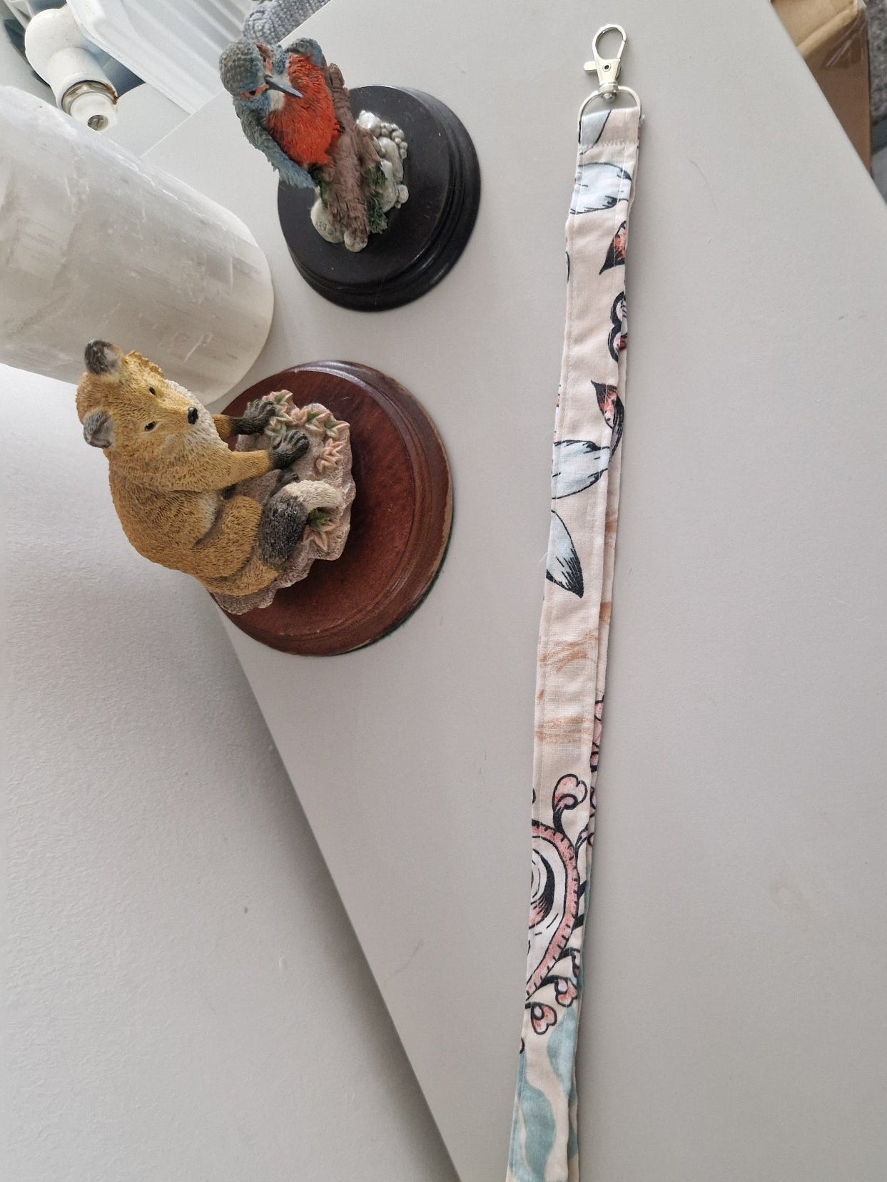 A fabric lanyard  with a multicolor floral and paisley pattern and silver metal hardware, laid out on a light gray tabletop.