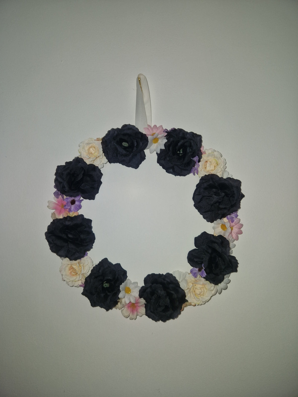 A circular floral hair clip or headband featuring large dark navy blue fabric roses, small cream-colored flowers, and a few light purple blossoms, attached to a clear plastic fastening clip on a plain light background.