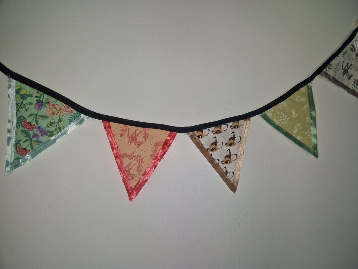 A string of triangular fabric bunting flags with different patterns and colors hangs against a plain light wall.