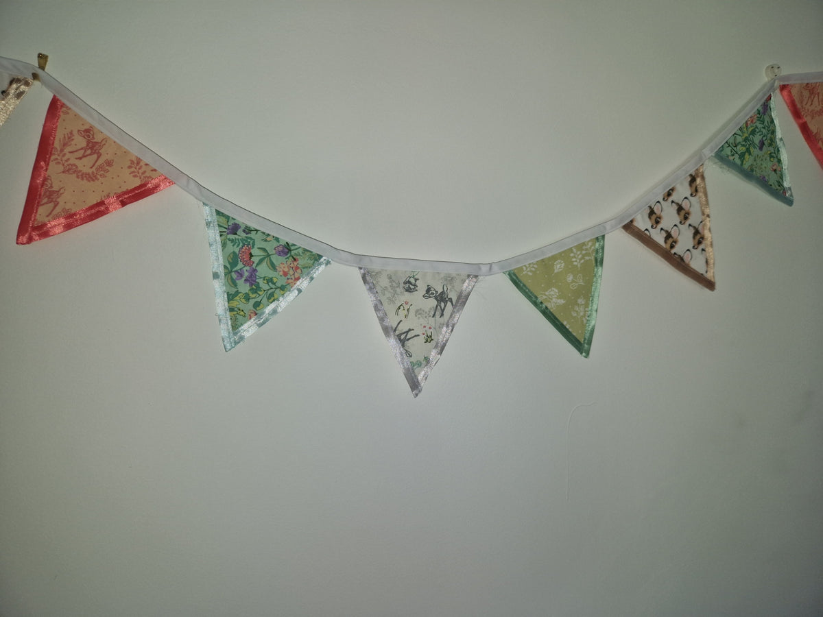 A string of triangular fabric bunting flags in assorted patterns and colors, hung against a plain light gray wall.