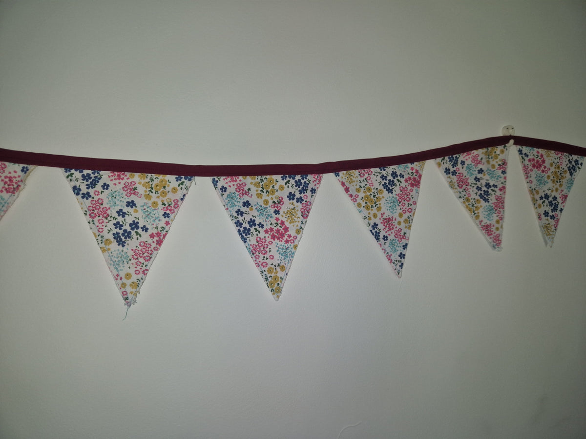 A string of triangular bunting flags with a colorful floral print hangs against a plain light gray wall.