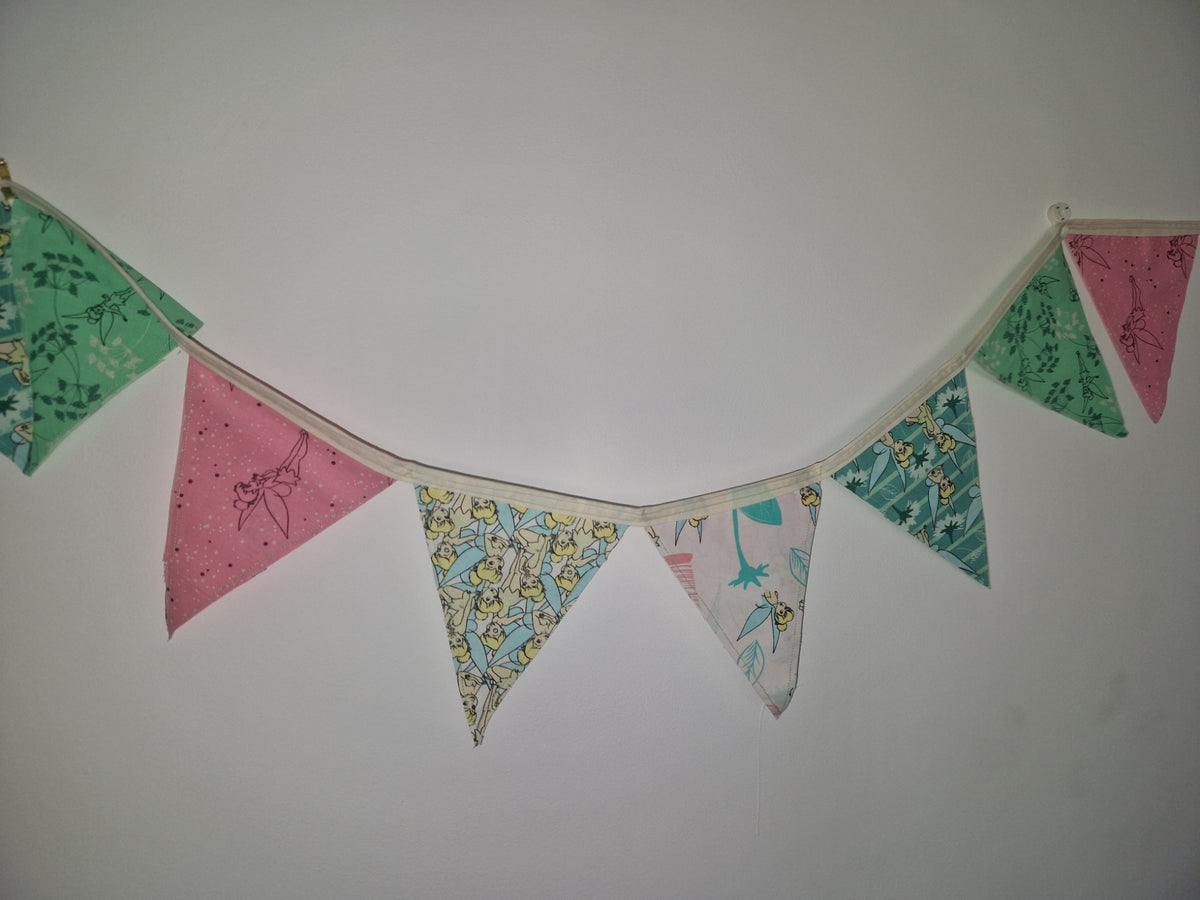 A fabric bunting banner with alternating pink and green patterned triangular flags hanging against a plain white wall.
