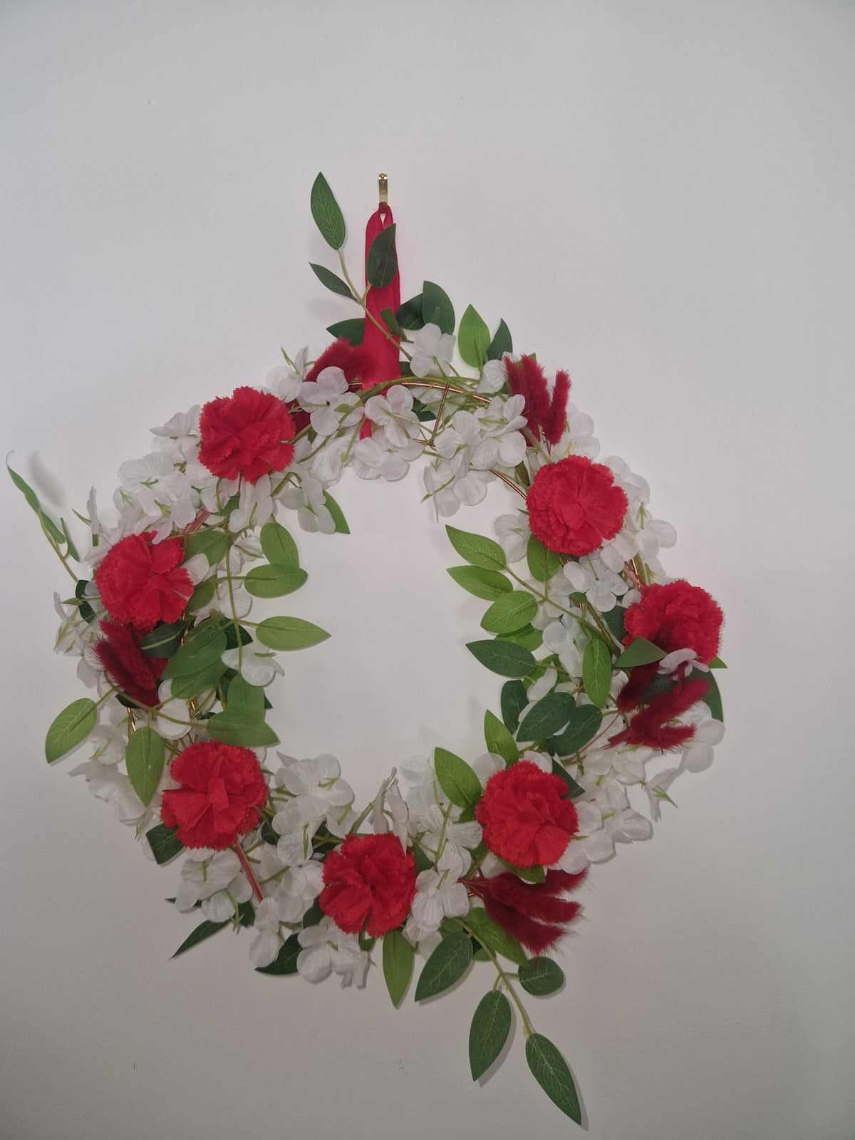 A decorative floral wreath featuring bright red roses, white blossoms, and green leaves, displayed against a plain light gray background.